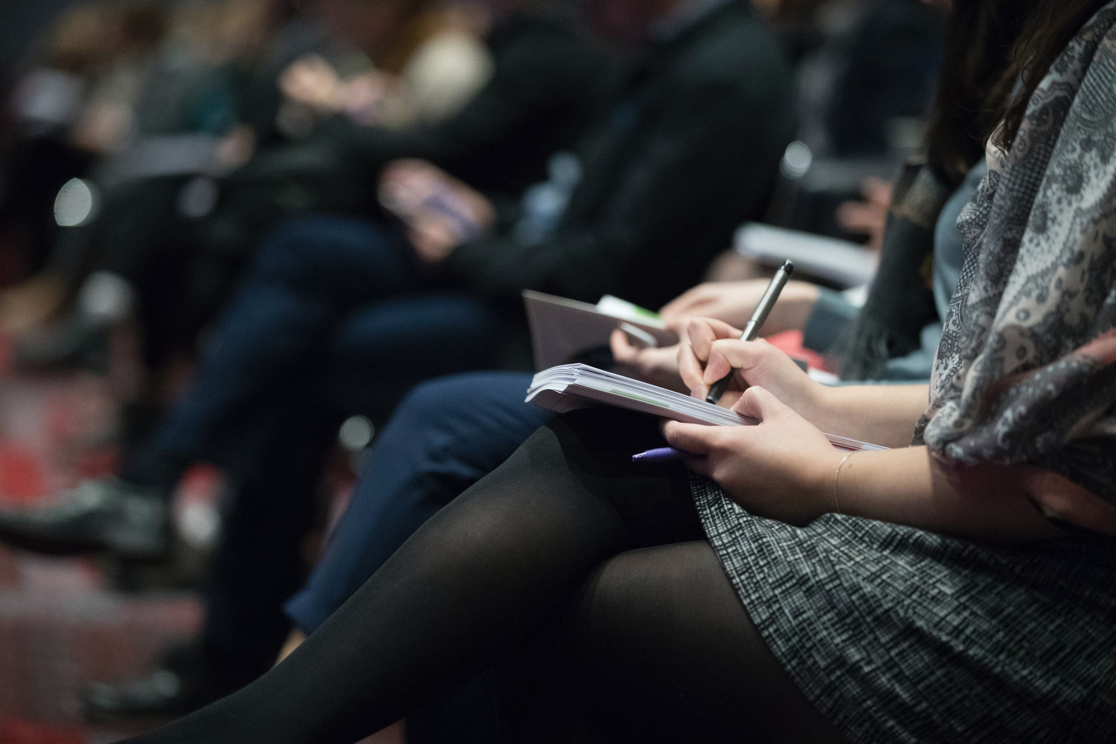 Vrouw noteert iets in een notitieboekje tijdens een plenaire bijeenkomst