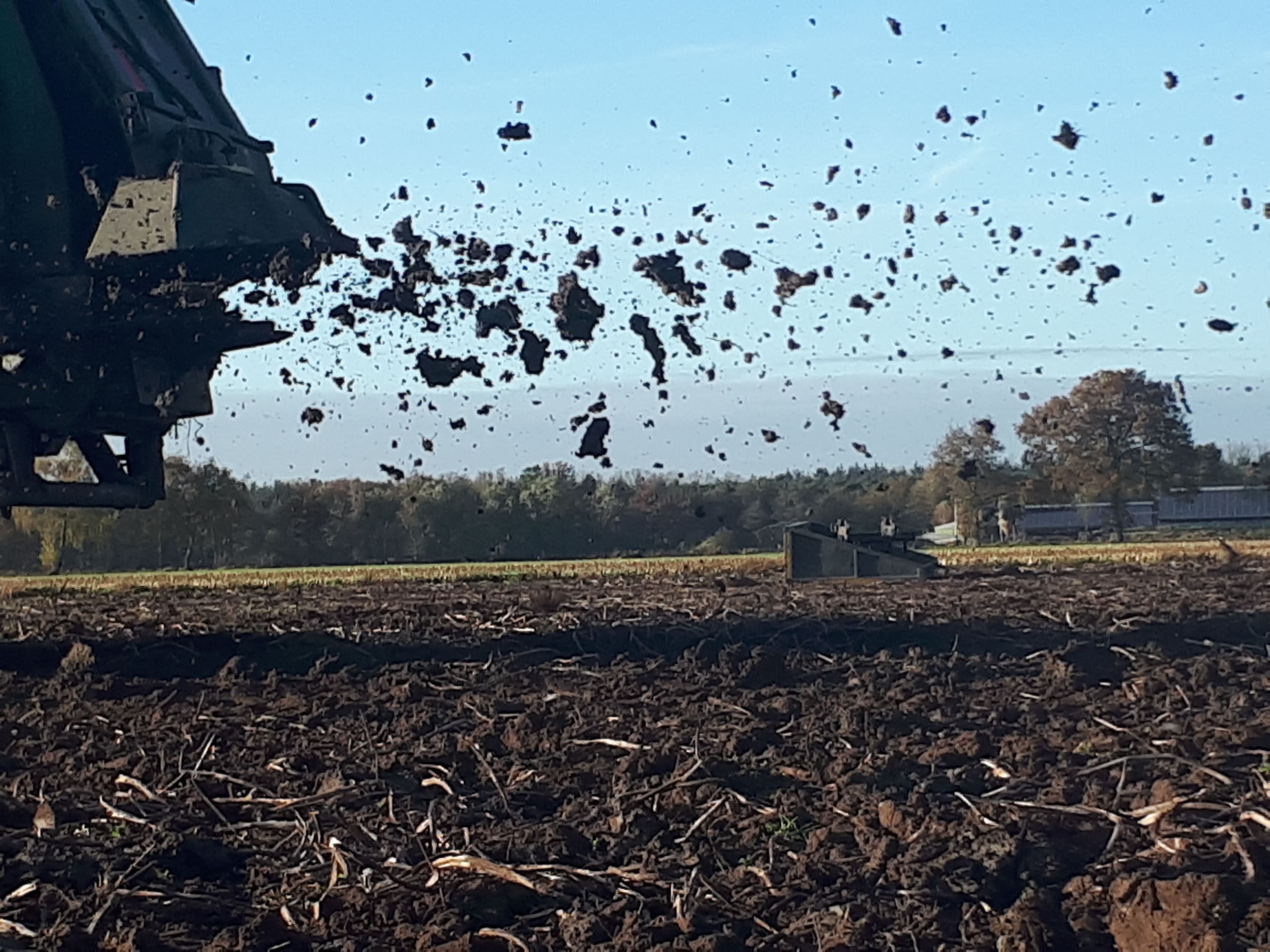 Klei wordt uitgestrooid achter een tractor op zanderige grond.
