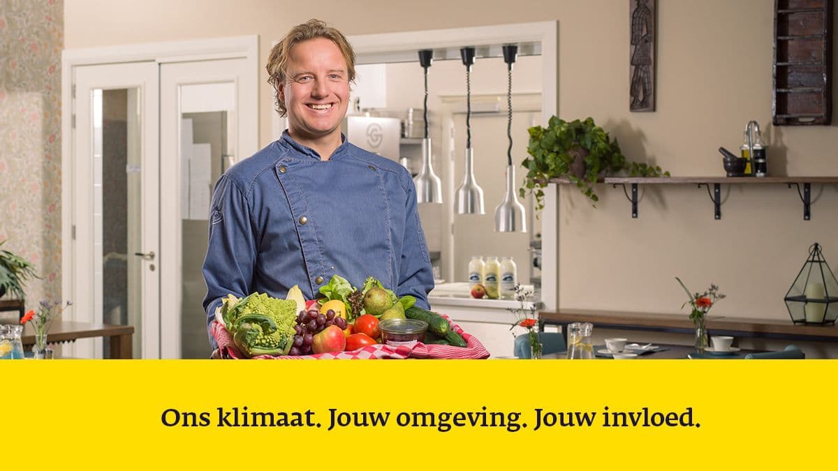 Man die glimlachend in de keuken staat met een enorme voorraad groenten
