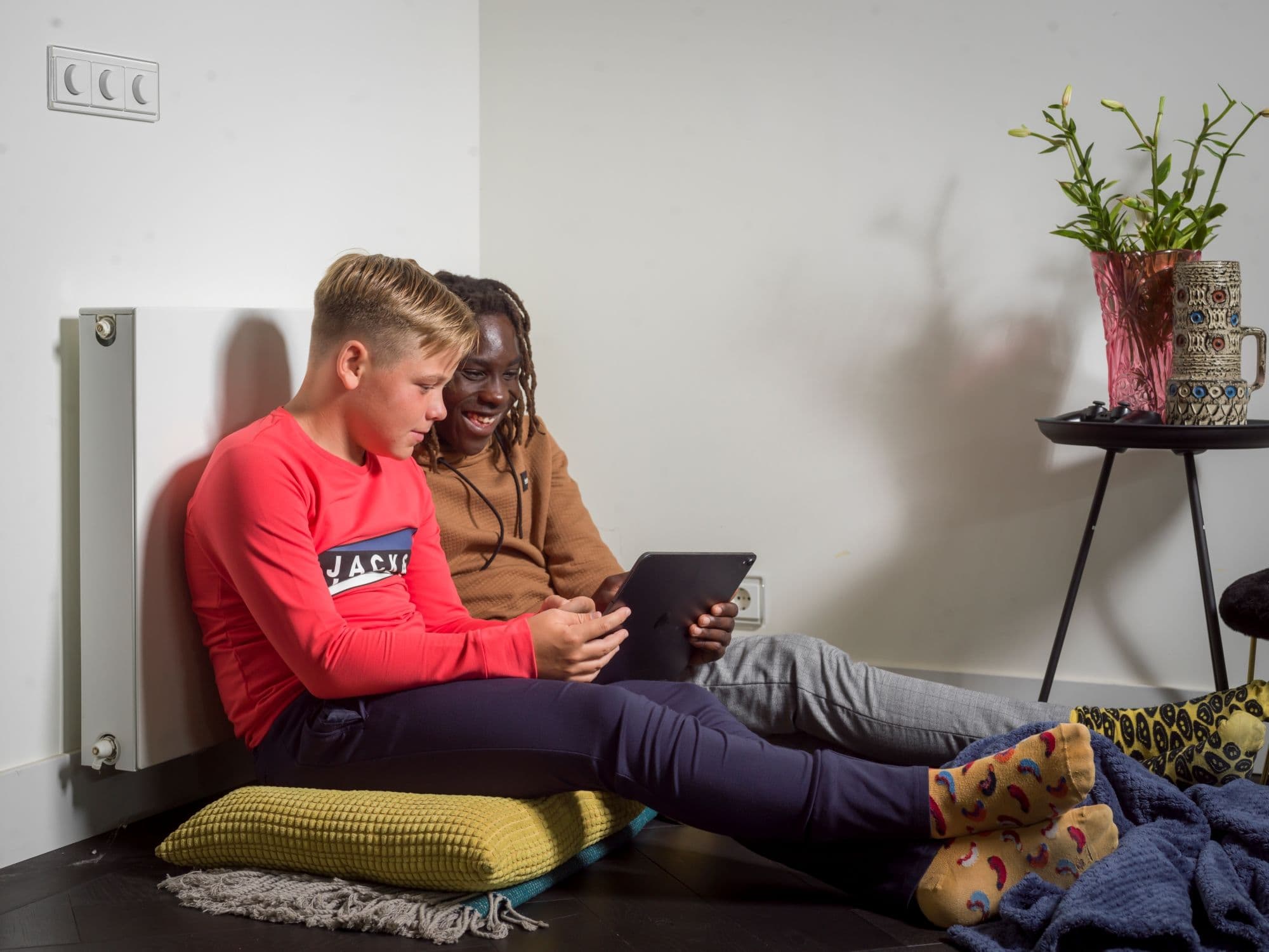 2 kinderen spelen op een tablet, zittend tegen een radiator