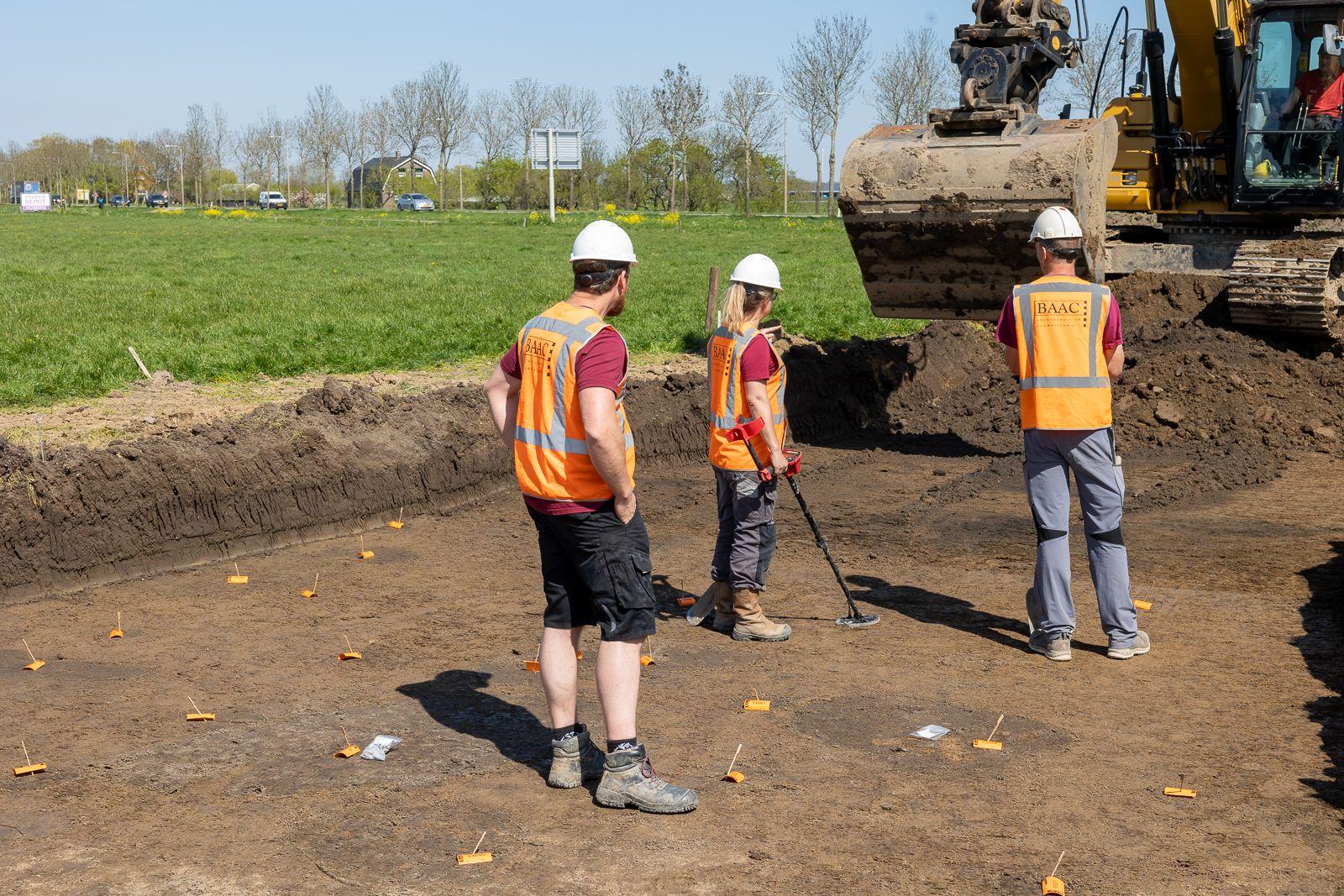 drie personen en een graafmachine zijn bezig met archeologische opgravingen