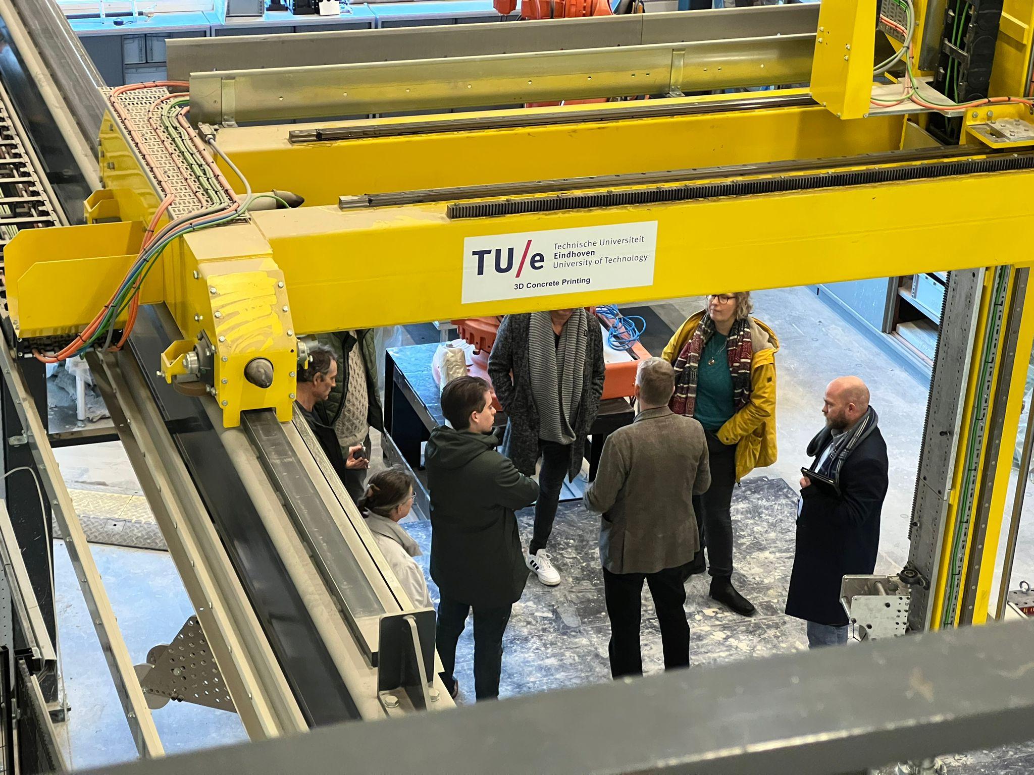 Mensen onder een 3D betonprint machine van de TU Eindhoven