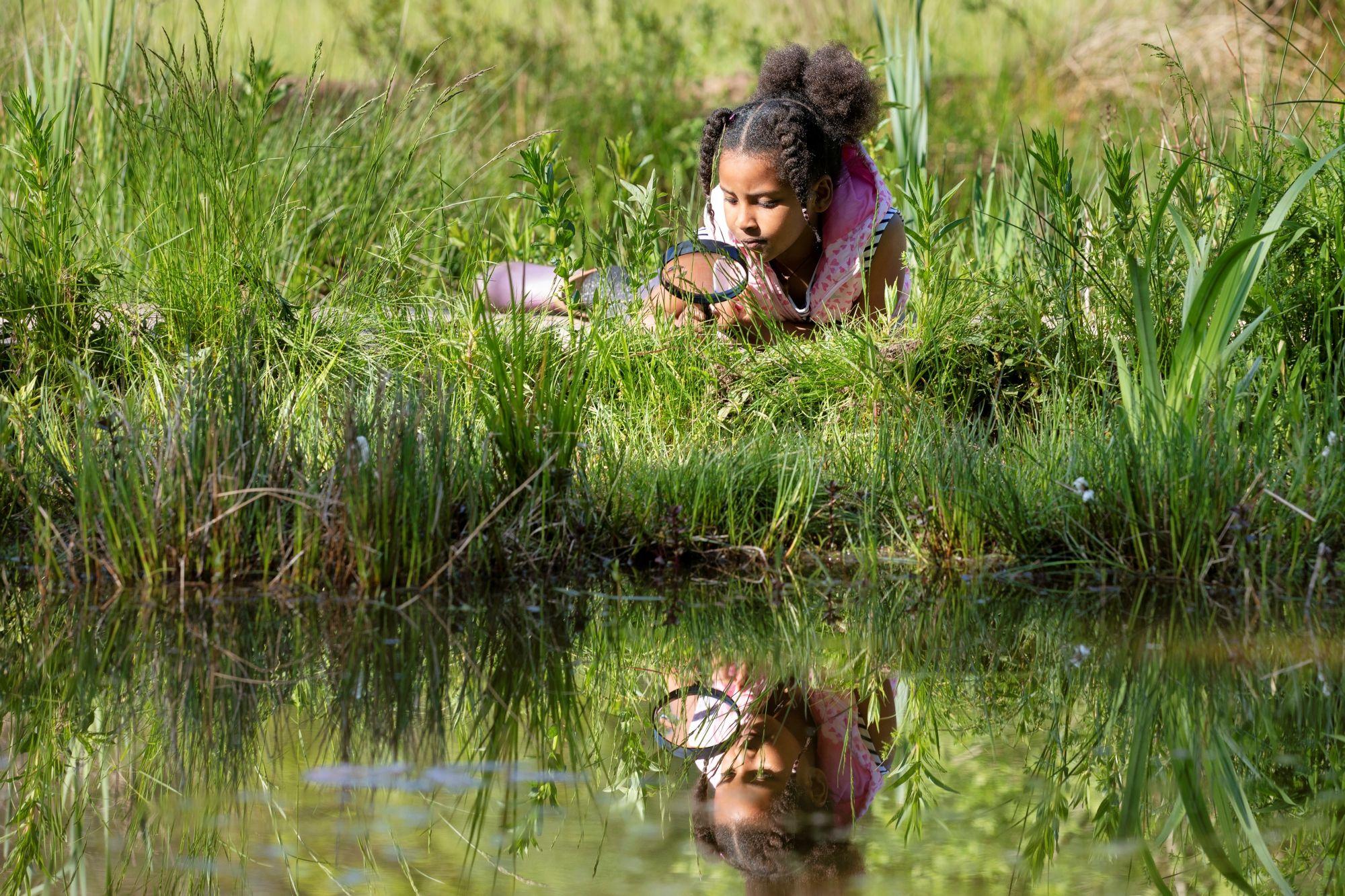 Meisje in het gras aan de waterkant met een vergrootglas